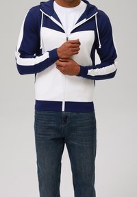 Felpa con cappuccio con zip blu marina e bianca, con blocchi di colore a contrasto, coulisse e polsini a costine. Abbinata a jeans denim scuri.