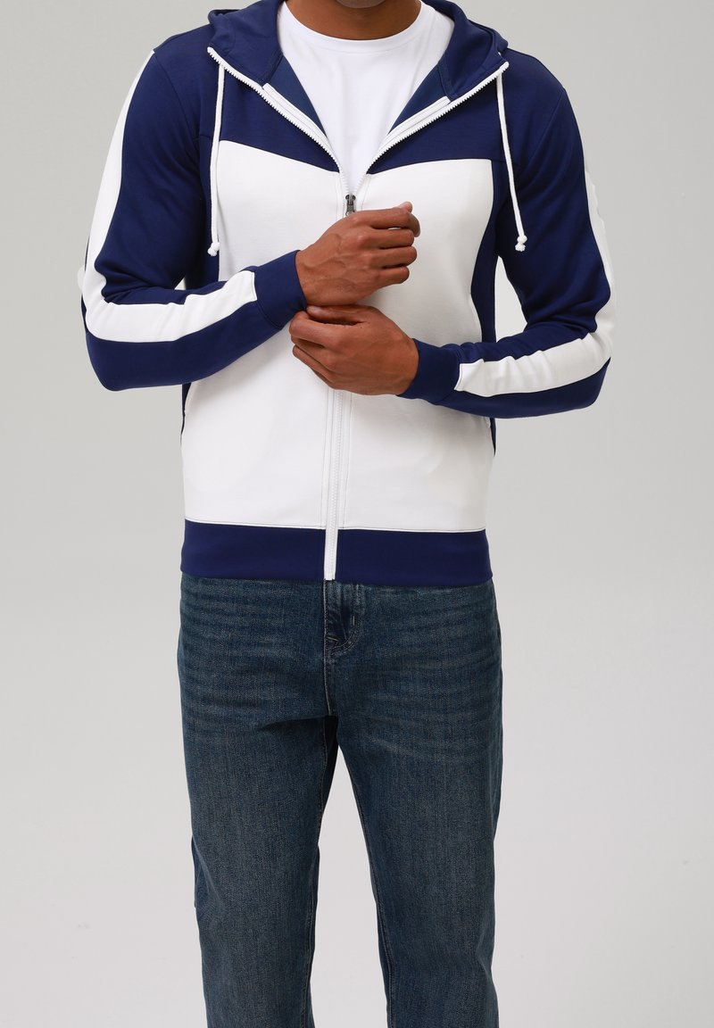 Felpa con cappuccio con zip blu marina e bianca, con blocchi di colore a contrasto, coulisse e polsini a costine. Abbinata a jeans denim scuri.