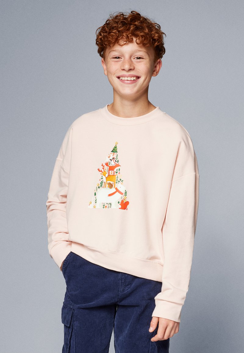 Sweatshirt rosa chiaro con maniche lunghe, caratterizzato da una grafica colorata di una scena natalizia che include animali e un albero. Pantaloni in velluto a coste blu scuro.