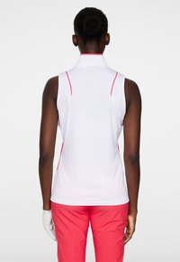 Ärmlös polo skjorta i vitt med rosa detaljer längs kragen och sidsömmarna. Tillverkad av mjukt, töjbart tyg för komfort.