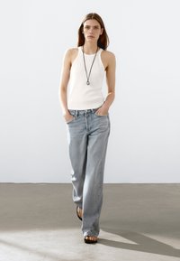 Witte mouwloze tanktop gecombineerd met lichtblauwe wijde jeans, met een relaxte pasvorm en subtiele wassing, en een ronde hangerketting.