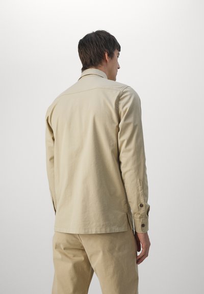 Beige long-sleeve shirt made of lightweight fabric, featuring a classic collar, button cuffs, and a straight hem. Simple design with no patterns.