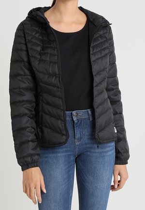 Sort pufferjakke med hætte, quiltet tekstur, lynlås lukning og elastiske manchetter. Båret over en sort top og blå jeans.