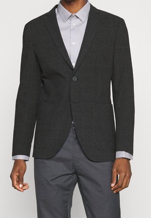 Blazer a quadri grigio scuro da uomo, con un design strutturato, dotato di chiusura a un bottone e due tasche frontali. Camicia con colletto grigio chiaro sotto.