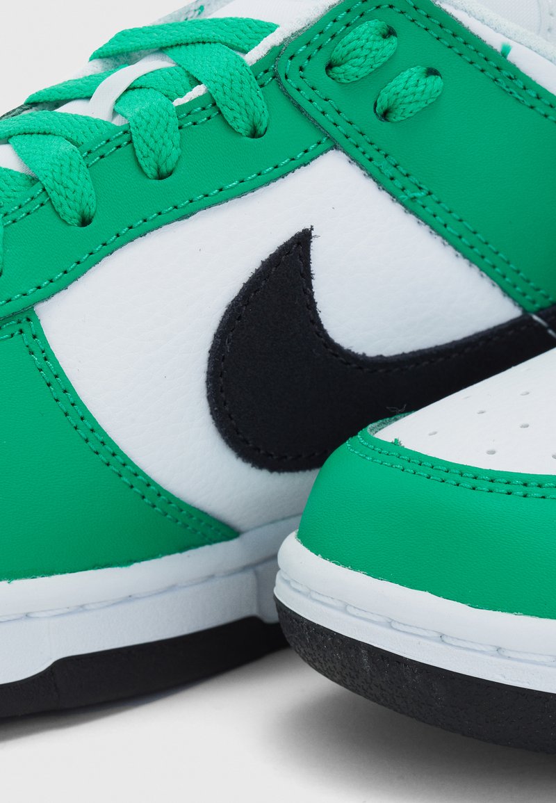 Zielono-białe sneakersy z czarnym logo Nike; posiadają teksturowaną skórę, okrągły czubek oraz płaską konstrukcję z wiązaniem.