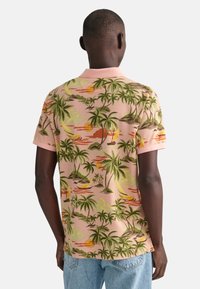 Pánská polokošile s krátkým rukávem v jemně růžové barvě s tropickým vzorem, který obsahuje zelené palmy, oranžové západy slunce a plachetnice. Klasický design límečku.