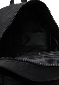 Interno di uno zaino nero che mostra il vano principale con fodera in tessuto e tasca interna con cerniera, cerniera parzialmente aperta.