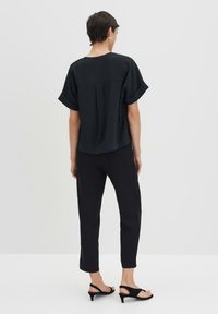 Top corto nero a maniche corte con vestibilità rilassata e piega sul retro, abbinato a pantaloni neri a gamba stretta e sandali con tacco aperti neri.