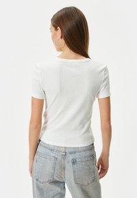 Hvid ribbet t-shirt med korte ærmer og rund hals, kombineret med lyseblå denimjeans med baglommer. Neutral farveskala.