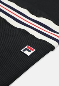 Primo piano di tessuto nero a coste con banda a strisce bianche, blu navy e rosse e una piccola patch logo quadrata con forme rosse e blu navy.
