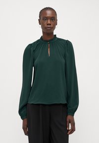 Forest green blouse with long, puffed sleeves, a high, ruffled neckline, and a keyhole opening. Smooth fabric, lightweight texture.