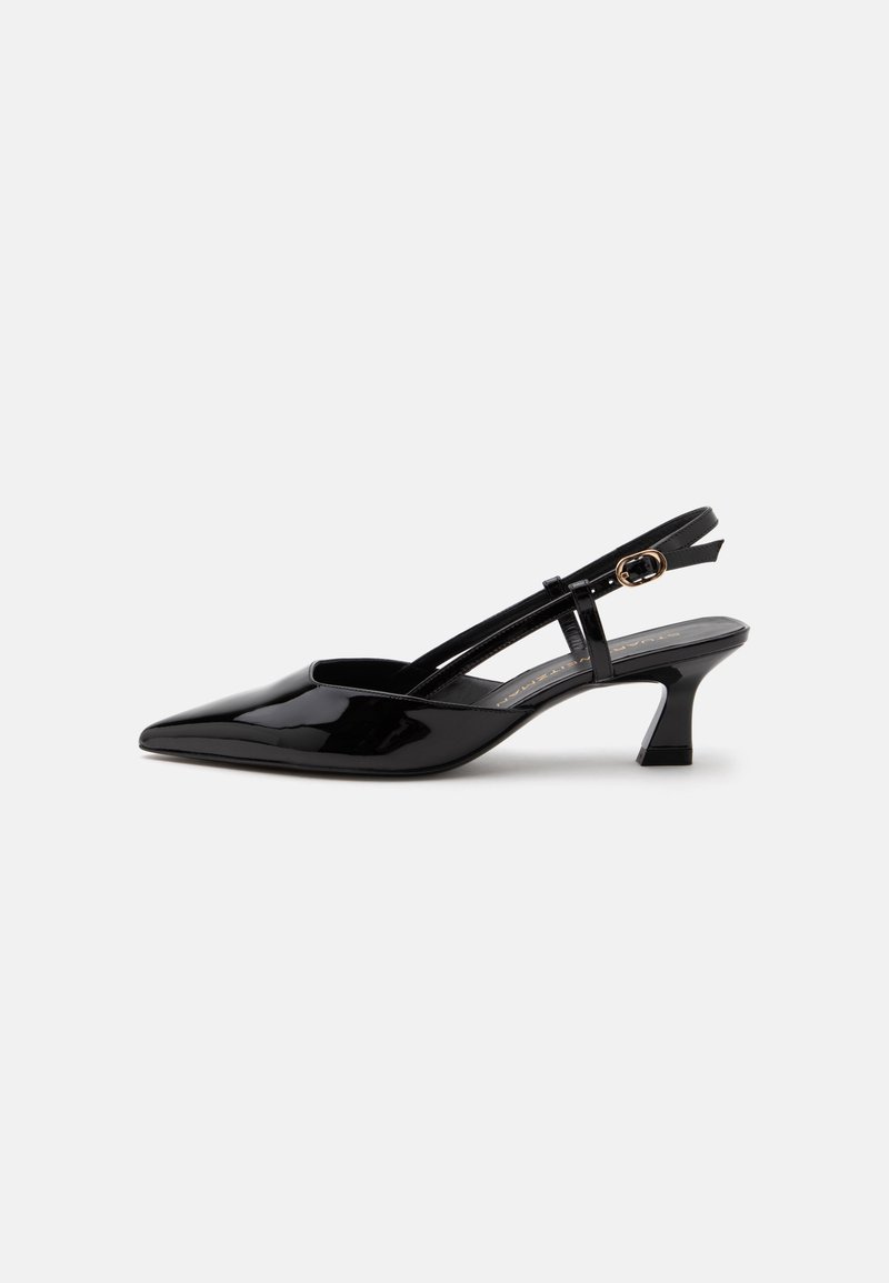 Chaussure slingback en cuir verni noir à petit talon, bout pointu et bride réglable avec boucle dorée sur fond blanc.