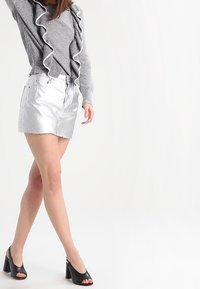 Šedý, nařasený top s dlouhým rukávem spárovaný s metalicky stříbrnou mini sukní. Černé sandály na vysokém podpatku doplňují outfit. Hladká textura po celé ploše.