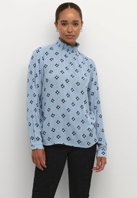 Blusa azzurro chiaro a maniche lunghe con colletto alto arricciato, caratterizzata da un motivo floreale nero e una vestibilità leggermente rilassata.