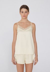 Camisole en satin crème avec un bord en dentelle au niveau de l'encolure, associé à un short assorti présentant des accents en dentelle sur les côtés.