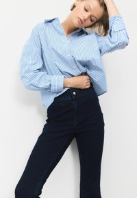 Blauw-wit gestreepte oversized button-up shirt met lange mouwen, gecombineerd met donkere skinny jeans, met een gladde textuur en een casual pasvorm.