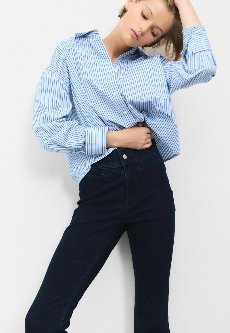 Blauw-wit gestreepte oversized button-up shirt met lange mouwen, gecombineerd met donkere skinny jeans, met een gladde textuur en een casual pasvorm.