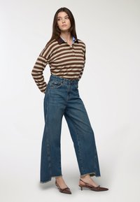 Polo a maniche lunghe a righe con un motivo marrone e crema, abbinato a jeans in denim blu a vita alta e gamba larga con orlo sfrangiato. Tacchi marroni.