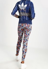 Marinblå bomberjacka med vita ränder och blommiga leggings. Leggings har ett flerfärgat blommönster, tillsammans med vita sneakers.