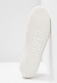 Vit sneaker med en slät yta, med en rosa detalj på sidan. Gummisulan har ett prickigt greppmönster och prägling med varumärket.