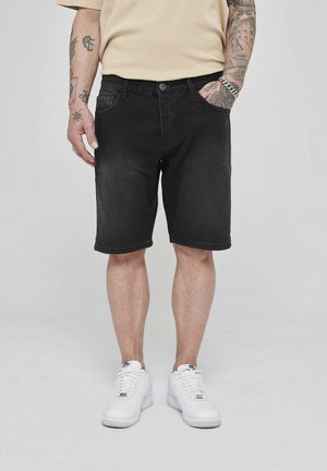 Black denim shorts with a straight leg, five pockets, and a button closure, paired with white sneakers on a neutral background.