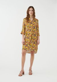 Abito a fiori giallo con accenti rossi e blu; maniche a tre quarti, vestibilità comoda, tessuto leggero, orlo all'altezza del ginocchio.