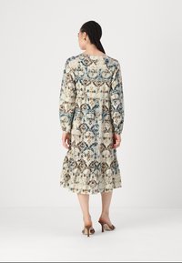 Μακρυμάνικο, εμπριμέ φόρεμα σε μπεζ απόχρωση με μπλε και καφέ λουλούδια, διαθέτει φαρδύ στρίφωμα και ελαστική μέση, συνδυασμένο με καφέ ψηλοτάκουνα.