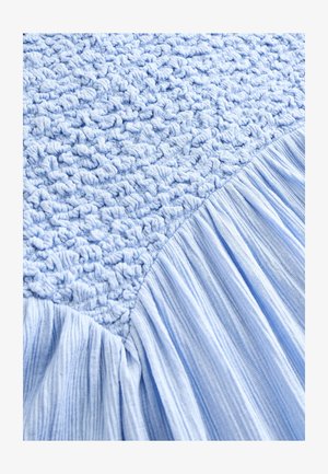 Světle modrá texturovaná tkanina s nařasenou, plisovanou částí a hladkým, zvrásněným povrchem. Materiál má jemnou, hmatovou kvalitu.