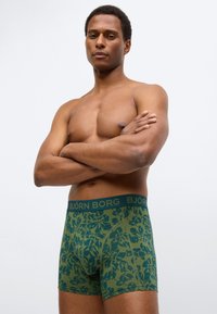 Μπόξερ σε ελιά πράσινο με λουλουδάτο μοτίβο, με αντίθετη σκουροπράσινη ζώνη μέσης με το λογότυπο "BJÖRN BORG". Λείο υλικό.