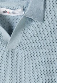 Polo tricoté bleu clair avec motif texturé respirant et col, affichant l'étiquette de la marque "minoti" et la taille pour enfants 4-5 ans.