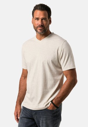 Camiseta de manga corta en tono beige claro con escote en V, hecha de una tela suave. Textura lisa, corte relajado, combinada con jeans de mezclilla oscura. Sin patrones visibles.