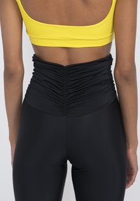 Black high-waisted leggings with gathered texture at the waist, paired with a yellow crop top featuring a wide neckline and solid color.