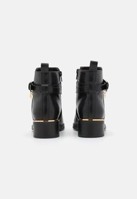 Bottines en cuir noir avec une finition texturée, fermeture éclair sur le côté et sangles décoratives. Présente un accent doré le long du talon.