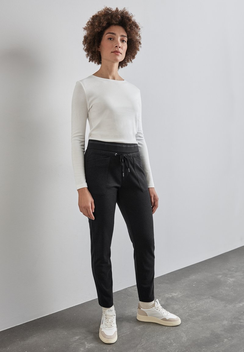 Top blanco de manga larga combinado con pantalones jogger negros con cintura elástica, bolsillos frontales y cordón. Llevado con zapatillas blancas.