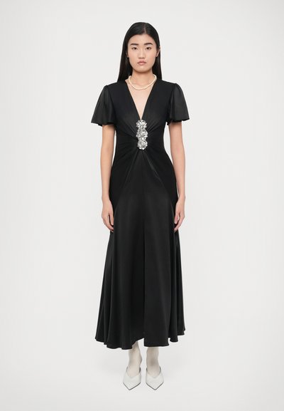 Black satin gown with short flutter sleeves, deep V-neck, and a floral silver embellishment at the waist. Notable A-line silhouette.