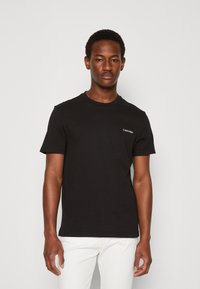 Sort kortærmet t-shirt lavet af bomuld, med rund hals og et lille hvidt logo på venstre bryst. Glat tekstur, klassisk pasform.