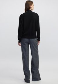 Zwarte lange mouw sweater met een ronde hals en geribbelde zoom, gecombineerd met losse, grijze wollen broeken. Zachte, gestructureerde stof.