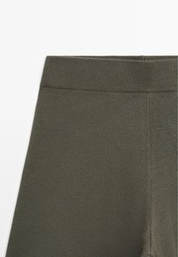 Leggings vert olive avec une ceinture côtelée, une texture douce et une finition lisse, sans motifs visibles ni détails métalliques.