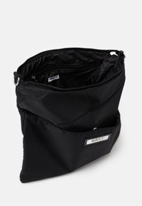 Borsa nera in nylon con chiusura a zip, dotata di una tasca interna e un'etichetta esterna. Texture liscia, design strutturato e look minimalista.