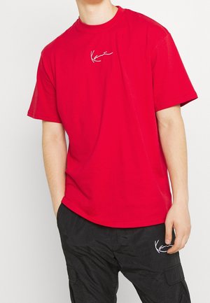 Rød bomulds T-shirt med korte ærmer, prydet med et hvidt broderet logo på brystet. Parret med sorte cargo bukser.