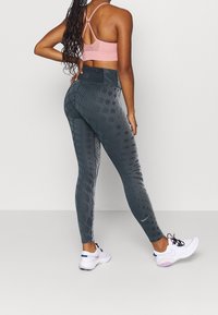 Vysoké šedé legíny s texturovaným vzorem a jemnými pruhy; v kombinaci s světle růžovým sportovním podprsenkou na tenkých ramínkách a bílými teniskami.