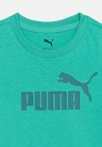 Τιρκουάζ μπλούζα με στρογγυλή λαιμόκοψη και σκούρο τιρκουάζ λογότυπο Puma και κείμενο στο κέντρο του στήθους.