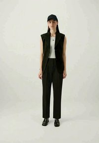 Μαύρο αμάνικο μπλέιζερ με μυτερά πέλματα, συνδυασμένο με καλοραμμένα μαύρα παντελόνια και λευκή ριμπ τακτοποιημένη μπλούζα. Μαύρο καπέλο και παπούτσια.