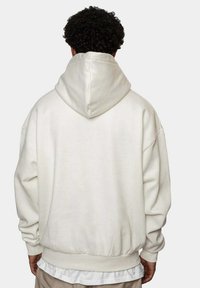 Hvit hettegenser med løs passform, som har kengurulomme og ribbede mansjetter. Glatt tekstur med et minimalistisk design.