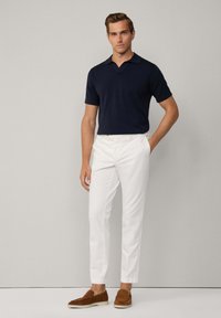 Polo a maniche corte blu navy, pantaloni slim-fit bianchi, scarpe slip-on marroni. Tessuto morbido, design del colletto classico, vestibilità sottile.
