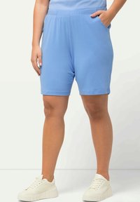 Ljusblå knälånga shorts i mjukt material med elastisk midja. Har sidofickor och är parat med klumpiga vita sneakers.