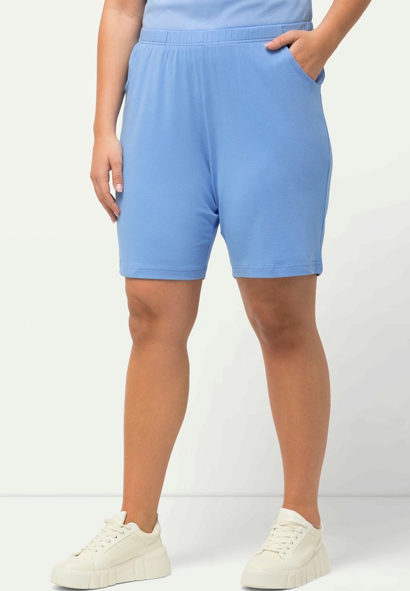 Ljusblå knälånga shorts i mjukt material med elastisk midja. Har sidofickor och är parat med klumpiga vita sneakers.