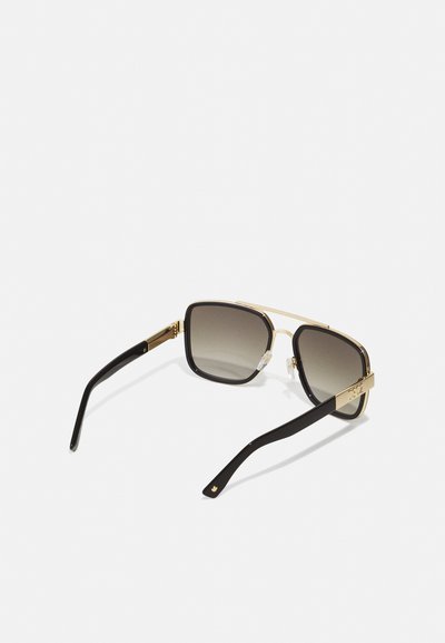 Quadratische Sonnenbrille mit einem goldenen Metallrahmen, schwarzen Acetatbügeln, dunklen Verlaufslinsen und auffälliger Markenkennzeichnung am Bügel.