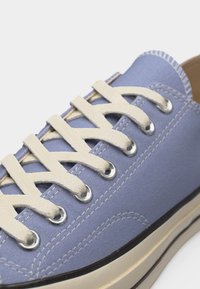 Baskets en toile bleu clair avec des lacets blancs passés à travers des œillets en métal et une semelle en caoutchouc blanche avec bordure noire.