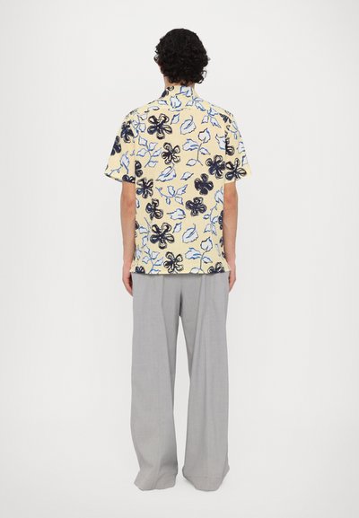 Short-sleeved, yellow shirt with a black and blue floral pattern, paired with light gray, wide-leg trousers. Back view, neutral background.
